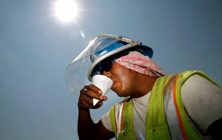 Persona trabajadora hidratándose bajo el sol, con casco, careta y chaleco reflectivo